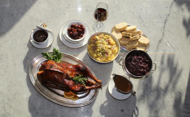 Ein festliches Mahl mit Gans, Rotkohl, Kartoffelsalat und Knödeln auf einem Marmortisch.