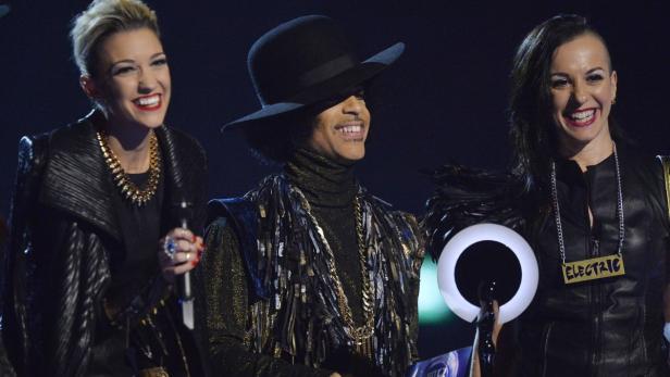 Prince mit zwei Backgroundsängerinnen auf einer Bühne.