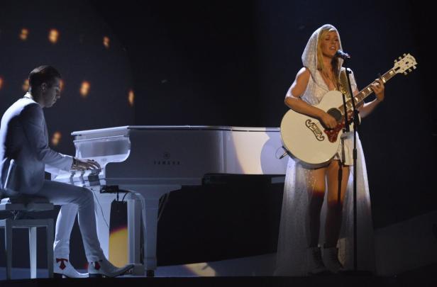 Eine Sängerin mit Gitarre und ein Pianist treten auf einer Bühne auf.