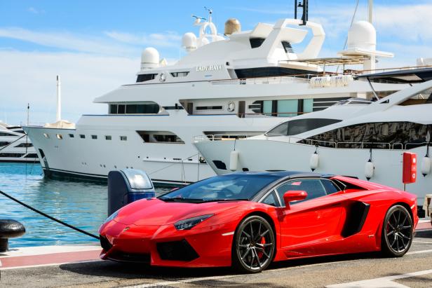 Ein roter Sportwagen steht vor mehreren Yachten im Hafen.