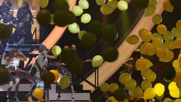 Pharrell Williams tritt mit Tänzern und Ballons auf einer Bühne auf.