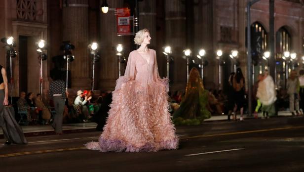 Eine Frau in einem rosa Federkleid auf einer Modenschau im Freien.