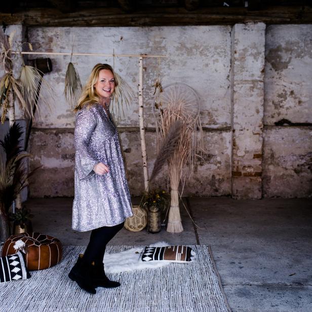 Eine Frau in einem Paillettenkleid posiert in einem Raum mit Boho-Dekoration.