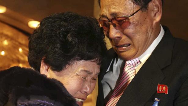 Ein weinendes älteres Paar, wobei der Mann eine Anstecknadel mit nordkoreanischen Führern trägt.