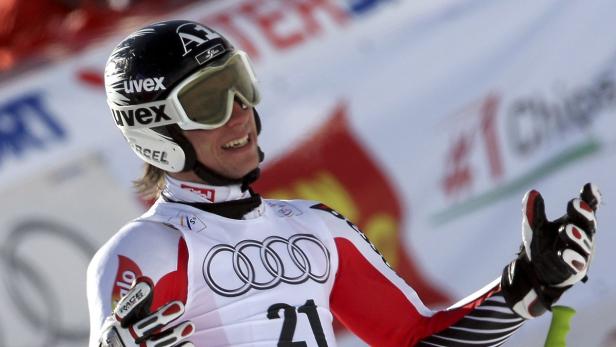 Ein Skirennläufer mit Helm und Skibrille jubelt mit erhobener Hand.