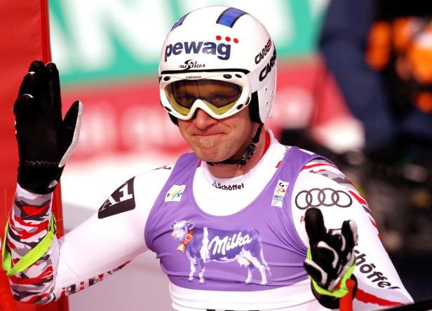 Ein Skirennläufer mit Helm und Skibrille winkt in die Kamera.