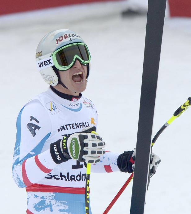 Ein Skirennläufer jubelt mit geöffnetem Mund und Skiern in der Hand.