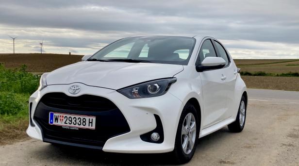 Ein weißer Toyota Yaris steht vor einer Landschaft mit Windrädern.