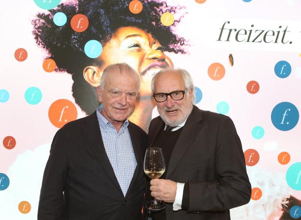 Zwei Männer posieren vor einem Hintergrund mit dem Wort „Freizeit“.