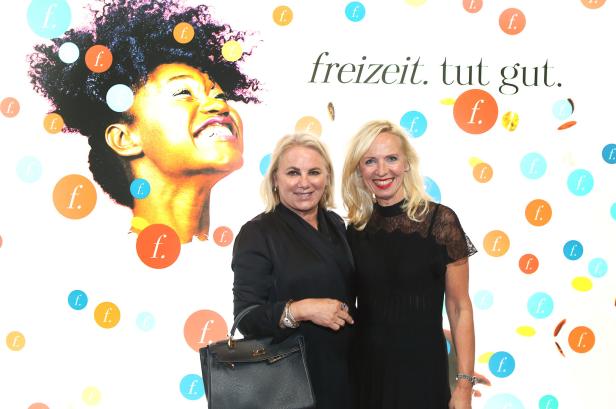 Zwei Frauen posieren vor einer Wand mit dem Schriftzug „freizeit. tut gut.“.