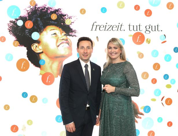 Zwei Personen posieren vor einem Hintergrund mit dem Slogan „freizeit. tut gut.“.