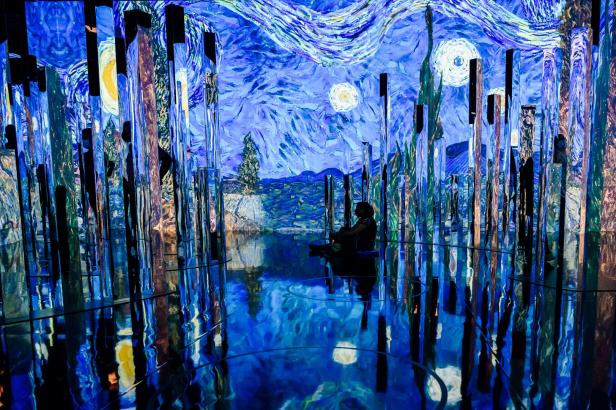 Eine Person sitzt in einem Raum, in dem „Sternennacht“ von Van Gogh projiziert wird.