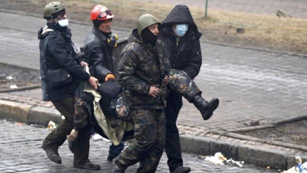 Mehrere Personen tragen eine verletzte Person in einem zerstörten Gebiet.