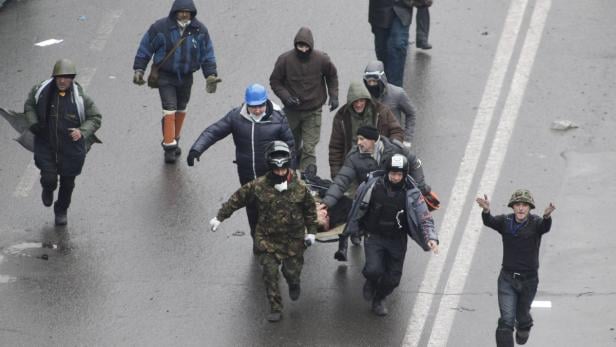 Mehrere Personen tragen eine verletzte Person auf einer Trage über eine nasse Straße.