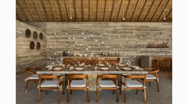 Ein gedeckter Esstisch in einem Raum mit Strohdach und Betonwänden.