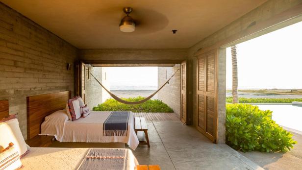 Blick aus einem Schlafzimmer mit zwei Betten auf eine Hängematte und den Strand.