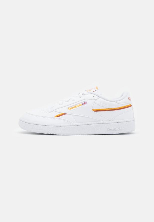Ein weißer Reebok Club C Schuh mit orangefarbenen und gelben Akzenten.