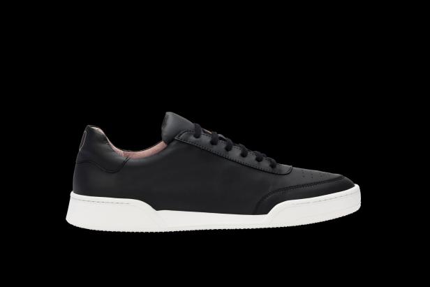 Ein schwarzer Ledersneaker mit weißer Sohle vor schwarzem Hintergrund.