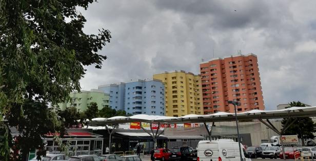 Mehrfarbige Wohngebäude ragen über ein Einkaufszentrum unter einem bewölkten Himmel auf.