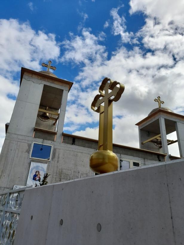 Eine Kirche mit einem goldenen Kreuz im Vordergrund unter blauem Himmel.