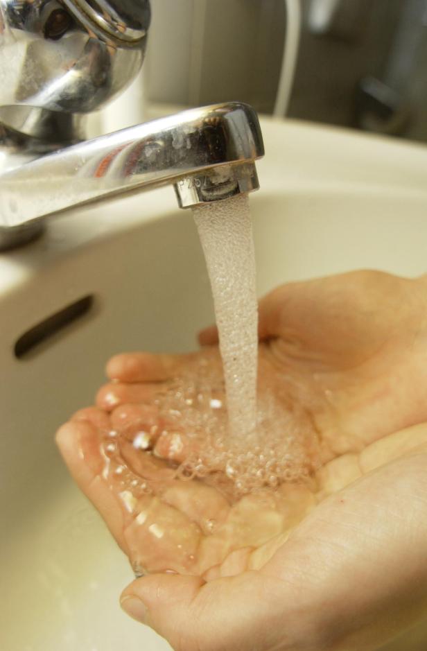 Eine Person hält ihre Hände unter einen laufenden Wasserhahn.
