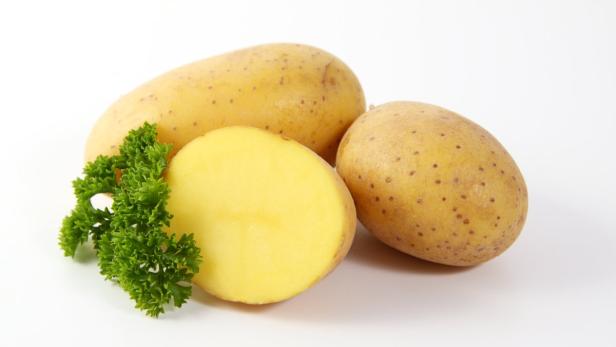 Drei Kartoffeln, eine davon halbiert, mit Petersilie auf einem weißen Hintergrund.