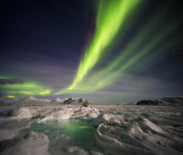 Grüne Nordlichter erhellen den arktischen Himmel über einer verschneiten Landschaft.