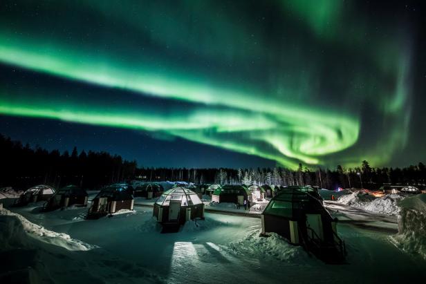 Nordlichter über einem Resort mit Iglu-ähnlichen Hütten im Schnee.