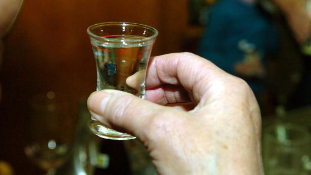 Eine Hand hält ein kleines Glas mit einer klaren Flüssigkeit.