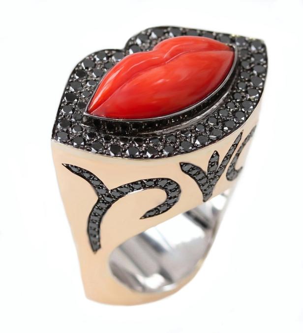 Ein goldener Ring mit einem roten Lippen-förmigen Stein und schwarzen Diamanten.