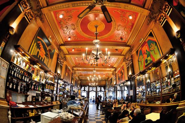 Innenansicht eines belebten, opulenten Cafés mit Kunstwerken und verzierten Decken.