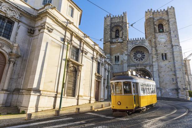 Eine gelbe Straßenbahn fährt vor der Kathedrale von Lissabon.
