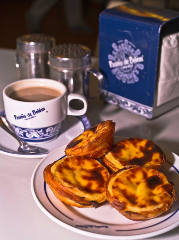 Eine Tasse Kaffee und vier Pastéis de Belém auf einem Teller.