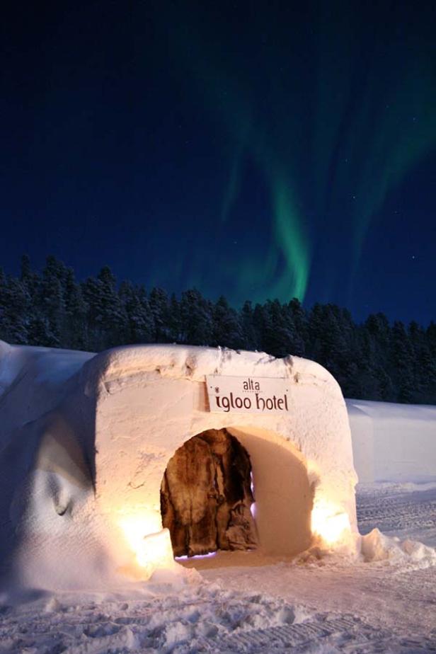 Das Alta Igloo Hotel unter dem Polarlicht in einer verschneiten Landschaft.