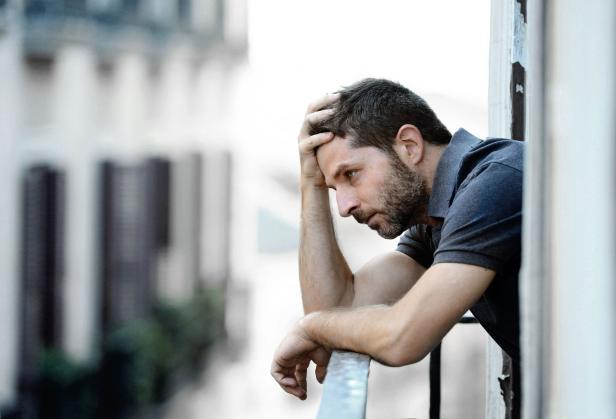 Ein junger Mann steht auf einem Balkon und leidet unter einer emotionalen Krise.