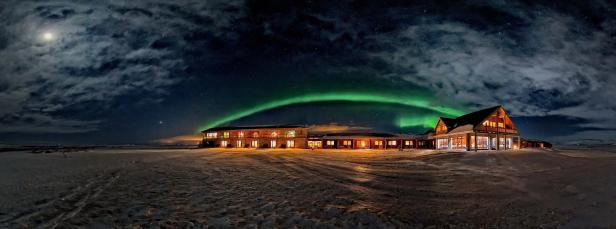 Ein Hotel unter dem Nachthimmel mit Nordlichtern und Mond.