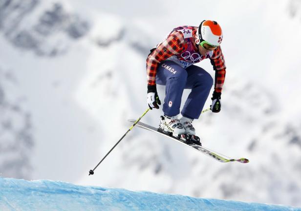 Ein kanadischer Skifahrer springt in der Luft vor schneebedeckten Bergen.
