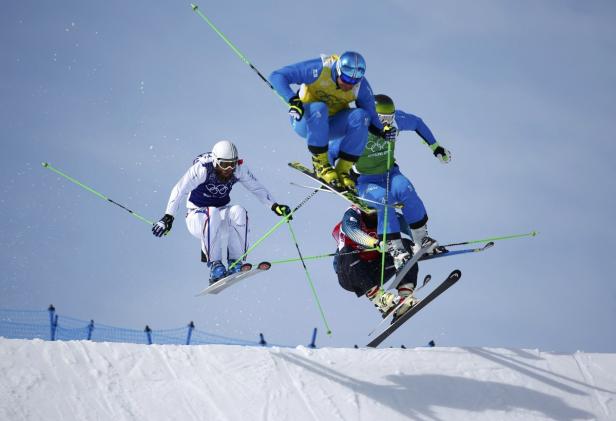 Mehrere Skifahrer springen während eines Skicross-Rennens über eine Rampe.
