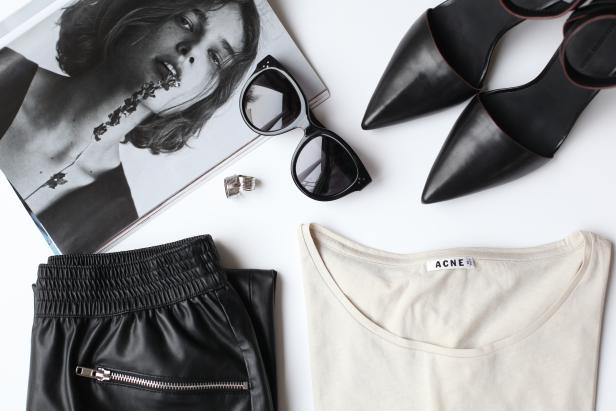 Ein Arrangement mit einer Zeitschrift, einer Sonnenbrille, Schuhen, einer Hose und einem Acne-T-Shirt.