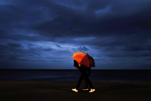 Zwei Personen gehen am Meer unter einem bunten Regenschirm spazieren.
