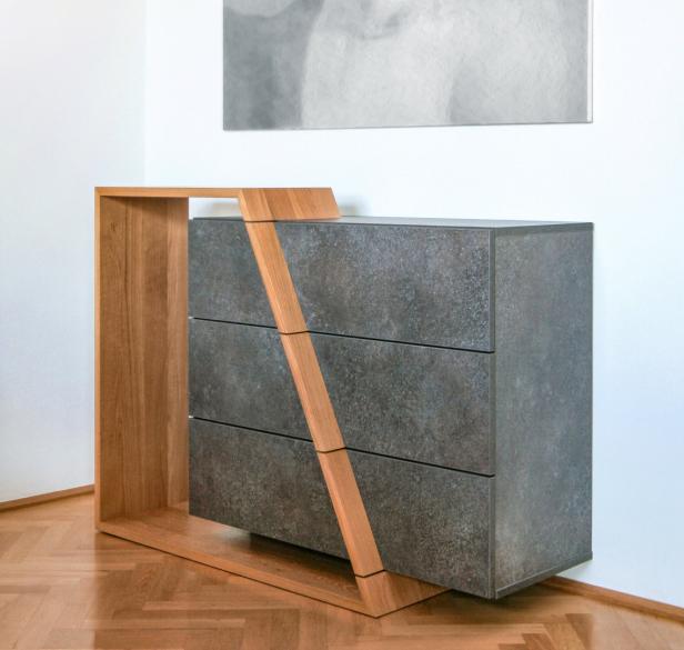 Eine moderne Kommode mit drei Schubladen und einem Rahmen aus hellem Holz steht in einem Raum.