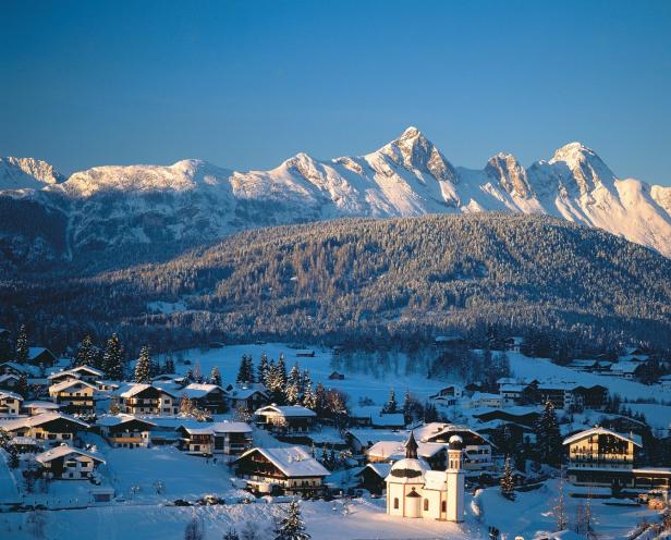 Ein verschneites Dorf in den Alpen mit einer beleuchteten Kirche im Vordergrund.