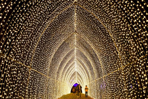 Ein Tunnel, der mit vielen kleinen Lichtern beleuchtet ist, durch den Menschen gehen.