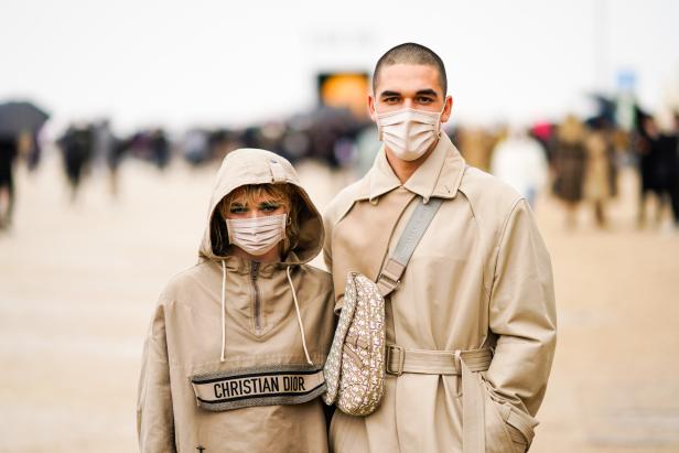 Zwei Personen mit Gesichtsmasken und beiger Kleidung der Marke Christian Dior stehen vor einer Menschenmenge.