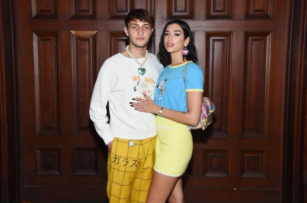 Dua Lipa posiert mit einem Mann vor einer Holztür.