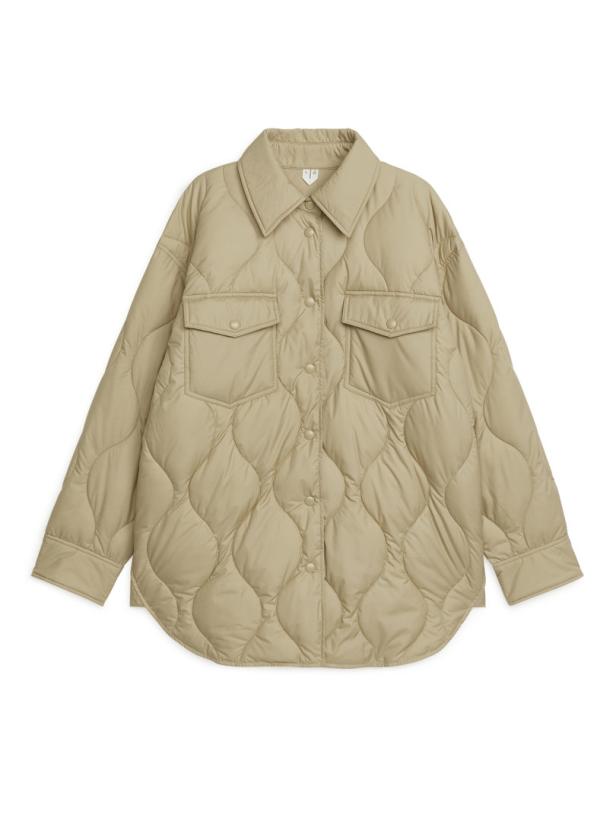 Eine gesteppte, hellbraune Hemdjacke mit zwei Brusttaschen vor einem weißen Hintergrund.