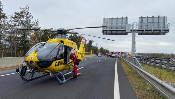 Ein gelber Rettungshubschrauber des ÖAMTC steht auf einer Autobahn neben Einsatzfahrzeugen.
