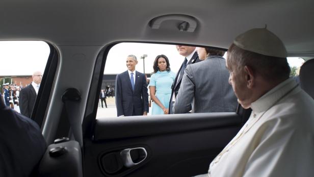 Papst Franziskus sitzt in einem Auto, während Barack und Michelle Obama draußen stehen.