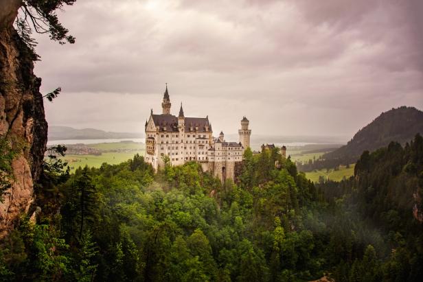 Blick auf Schloss Neuschwanstein im Nebel, rundherum viel Wald und Natur
