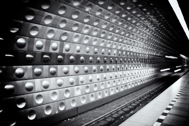 Schwarz-Weiß-Aufnahme einer U-Bahn-Station mit einer Wand aus Blöcken mit runden Vertiefungen.